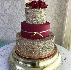 a three tiered wedding cake with red roses on top and gold trimmings