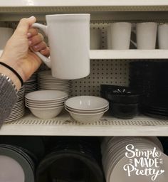 a person is holding a coffee mug in front of plates and cups on the shelf