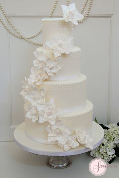 a three tiered white wedding cake with flowers on the side and pearls around the edges