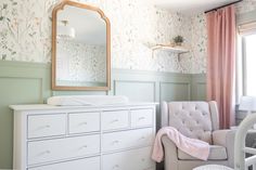 a baby's room with pink and green wallpaper, white furniture and a large mirror on the wall