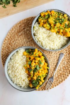 two bowls filled with rice and vegetables on top of a mat next to a fork