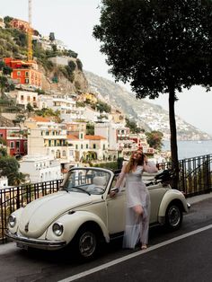 a woman in white dress standing next to an old car