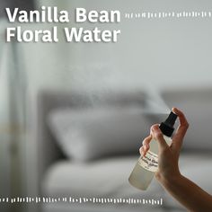 a hand holding a bottle of vanilla bean floral water in front of a white couch