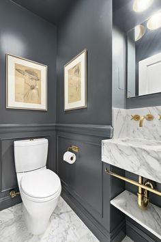 a white toilet sitting next to a sink in a bathroom under two framed pictures on the wall