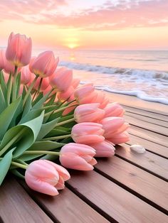 a bunch of pink tulips sitting on top of a wooden table next to the ocean