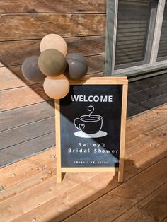 a welcome sign with balloons in front of a wooden wall and door on the side of a building