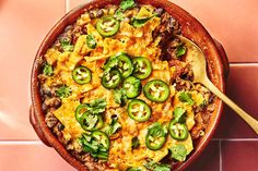 a casserole dish with green peppers, cheese and meat in it on a pink tiled surface