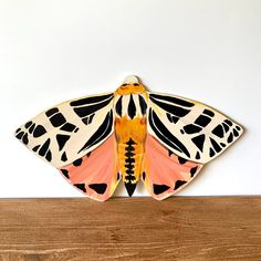 a large orange and black moth sitting on top of a wooden table next to a white wall