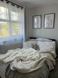 an unmade bed with white blankets and lights on the windowsill in a bedroom