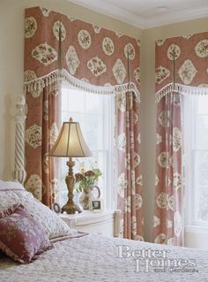 a bedroom with pink and white bedding, window curtains and lamp in the corner