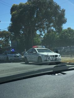 two police cars are parked on the side of the road in front of a fence