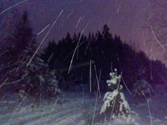 the night sky is lit up with snow and trees in the foreground, while stars streak across the sky