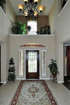 a foyer with a rug, chandelier and potted plants