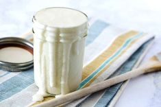 a glass jar filled with white liquid sitting on top of a striped cloth next to a wooden spoon