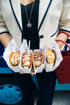 a woman holding three different types of hotdogs in paper containers with condiments