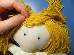 a hand is holding the ends of a yellow doll