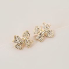 Gold stone-studded ribbon earrings. Sterling Silver 10k Gold Plated Measurements: 0.68in x 0.58in / 1.72cm x 1.47cm Formal Bow Earrings With Cubic Zirconia, Formal Bow Earrings In Cubic Zirconia, Elegant Cubic Zirconia Earrings With Bow, Gold Ribbon Earrings, Yellow Gold Cubic Zirconia Star Earrings, Rhinestone Bow Earrings, Gold-plated Sterling Silver Butterfly Earrings, Ribbon Earrings, Gold Stone