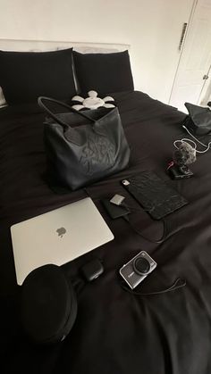 an apple laptop, cell phone and other items are on a bed with black sheets