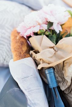 a bottle of wine sitting on top of a bed next to some paper and flowers