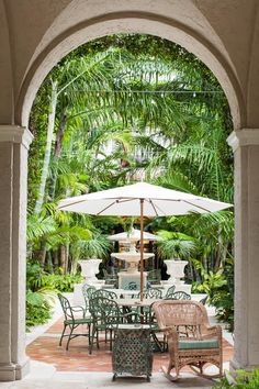 an outdoor dining area with chairs, umbrella and table in the center surrounded by palm trees