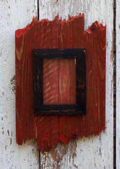 an old red and black frame hanging on a white wooden wall with paint peeling off it