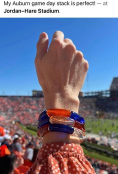 a person with their hand up in the air at a football game, wearing bracelets that read'my auburn game day stack is perfect @ jordan - hare stadium