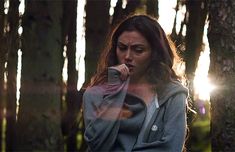 a woman standing in the woods with her hand on her mouth