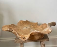 a wooden bowl sitting on top of a wooden stool next to a white wall and floor