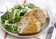 two pieces of meat on a plate with spinach leaves and fork next to it