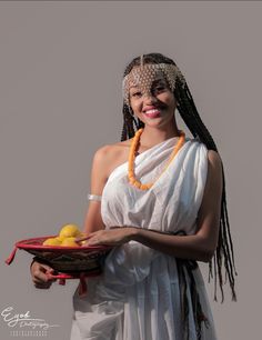 a woman holding a basket filled with lemons and wearing a headdress while smiling