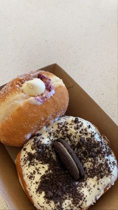 two donuts with white frosting and chocolate sprinkles in a box