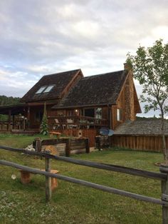 a wooden house sitting on the side of a lush green field next to a fence