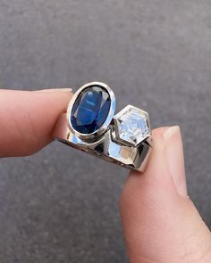 someone is holding their engagement ring with blue stone in it's center and two diamonds on the side