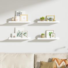 three white shelves on the wall above a couch with pictures and plants in them,