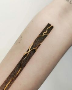 a close up of a person's arm with a gold and black tattoo on it