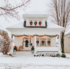 a white house decorated for christmas with wreaths on the front porch and lights hanging from the roof