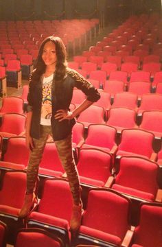 a woman standing in front of an empty theater seat with her hands on her hips