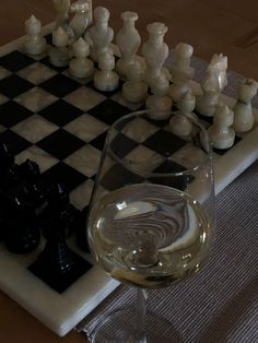 a glass of wine sitting on top of a chess board next to a set of black and white pieces