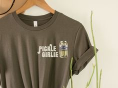 "Express your love for pickles in style with our charming \"Pickle Girlie\" T-shirt. Designed for pickle enthusiasts, this shirt proudly showcases the playful phrase \"Pickle Girlie,\" making it a delightful choice for those who adore all things pickled. Whether you're a pickle lover yourself or looking for a unique gift for someone who shares this passion, this shirt is sure to bring a smile. Crafted with care, this t-shirt combines comfort and fun, allowing you to show off your pickle obsession with pride. HOW TO ORDER 1. Check and review all photos (including colors and sizes) 2. Select Your tshirt size and t-shirt color from drop down menu 3. Select quantity 4. Click ADD TO CART. For multiple items go back and repeat. IF THE ITEM HAS CUSTOMIZATION Make sure to specify in the customizat Pickle Shirt Ideas, Olivia Art, Pickle Lover, Pickle Jar, Homemade Pickles, Trendy Shirt Designs, Business Checks, Friend Gifts, Things To Buy