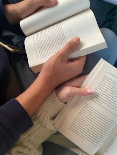 a person sitting down reading a book with their hands on top of each other's books