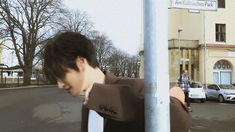 a young man leaning against a pole on the street