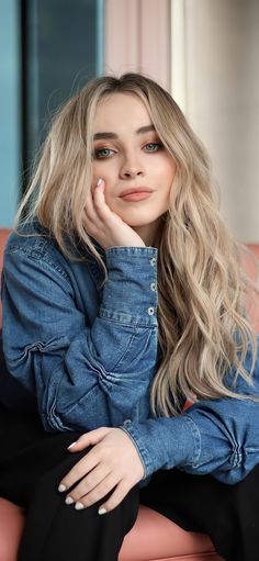 a woman sitting on top of a pink couch wearing a denim shirt and black pants