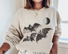 a woman wearing a sweatshirt with bats on it and the moon in the sky behind her