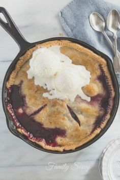 a blueberry pie with ice cream in a cast iron skillet on a marble surface