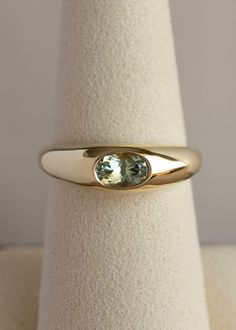 a yellow gold ring with an oval shaped green sapphire stone on the center, sitting on top of a white cloth