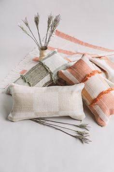 three pillows and two plants on a white tablecloth with an orange striped pillow behind them