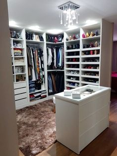 a walk in closet filled with lots of white shelves and drawers next to a bed