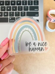 someone holding up a sticker that says be a nice human with a rainbow on it