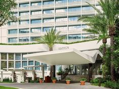 the entrance to a hotel with palm trees and potted plants in front of it