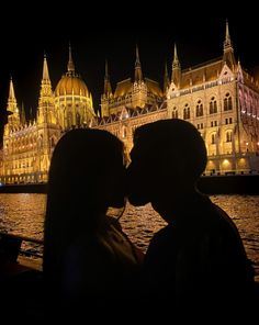 a man and woman kissing in front of a large building with lights on it's sides